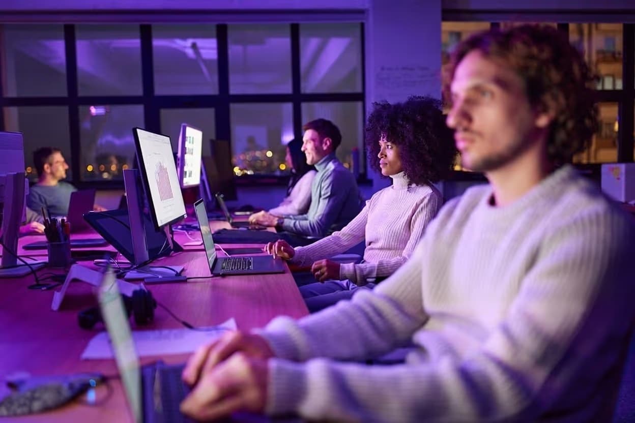 A team of diverse professionals working at desks in a modern, neon-lit office at night, focusing on computer screens with data charts, symbolizing the technological revolution and data-driven future of the global lottery. The Digital Engine of Modern Lottery Innovation